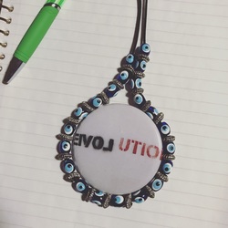 Picture of a button with the word Revolution (with the word LOVE in reverse highlighted), surrounded by a string of small dark blue beads with an eye painted on each of them.