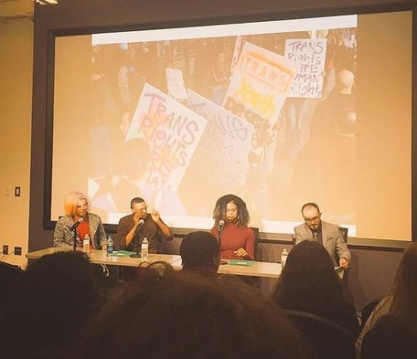 Picture of a panel sitting in front of a screen showing an image from a trans-themed protest. The panelists are Reina Gossett, Holiday Simmons, Raquel Willis, and T.J. Jourian