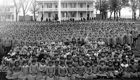 Picture of hundreds of Indigenous children posing for the camera, with a school building behind them