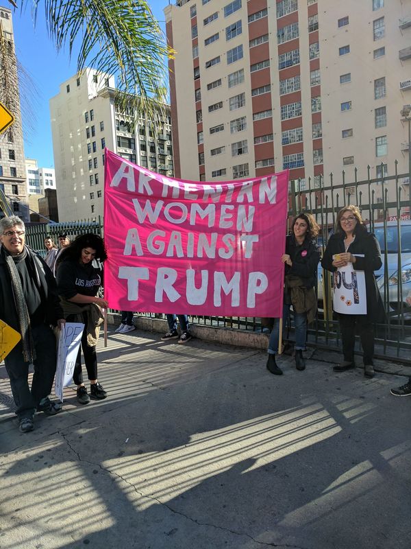 Four individuals stand near or hold a large pink sign saying 