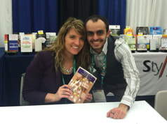 Sonja Ardoin and T.J. Jourian pictured together behind a table. Sonja is holding a copy of her book 